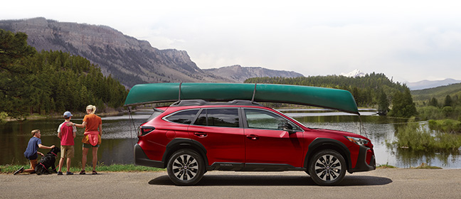 Subaru Outback parked in front of lake, family with dog looking ahead.